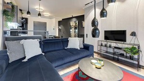 Ein modernes Wohnzimmer mit einem dunkelblauen Sofa, einem runden Couchtisch und einem Fernseher auf einem schwarzen Schrank.