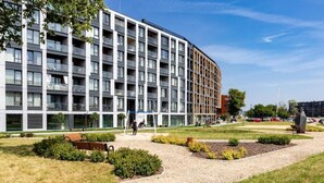 Ein modernes Gebäude mit einer gewölbten Fassade, mehreren Balkonen und einem begrünten Innenhof mit Wegen und Bänken.
