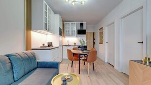 Ein modernes Wohnzimmer mit einer Couch, einem Esstisch mit Stühlen, einer Küchenzeile und einem an der Wand befestigten Fernseher.