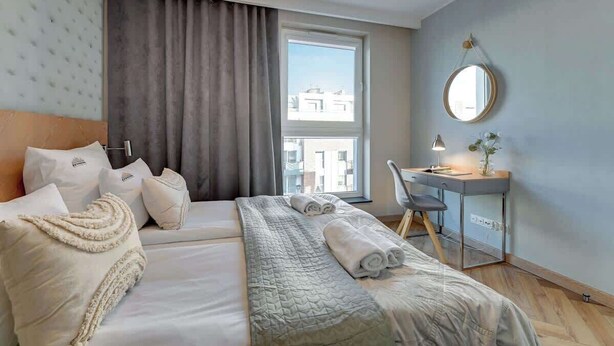 A hotel room with a bed, a desk, a chair, a round mirror, and a window with a view of buildings. - Angielska Grobla 51A | Near Old Town & Marina (Gdańsk)