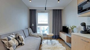 A modern living room with a sofa, a small round table, a white furry rug, a TV, and a kitchen area with a microwave. - Angielska Grobla 51A | Near Old Town & Marina (Gdańsk)