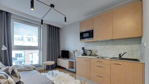 A modern apartment with a kitchenette, a sofa with patterned cushions, a white furry rug, and a large window with curtains. - Angielska Grobla 51A | Near Old Town & Marina (Gdańsk)