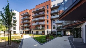 Ein modernes Mehrfamilienhaus mit mehreren Balkonen, einem gepflasterten Innenhof und Sitzgelegenheiten im Freien.