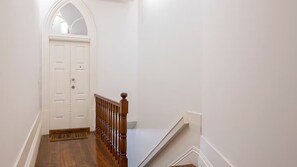 A narrow hallway with a wooden staircase leading to a white door with a decorative arch. - Mouzinho 120 | Stylish Studio by LovelyStay (Porto)