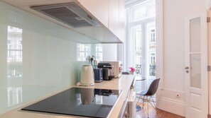 A modern kitchen with a large induction cooktop, a coffee machine, and a view of the city through large windows. - Mouzinho 120 | Stylish Studio by LovelyStay (Porto)