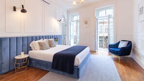 Ein Schlafzimmer mit einem großen Bett, einem blauen, gepolsterten Kopfteil, einem Nachttisch mit einer Kerze und einem blauen Sessel.