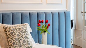 Ein Zimmer mit einem blauen, gepolsterten Kopfteil, einem weißen Kissen mit Blumenmuster und einer Vase mit roten Tulpen.