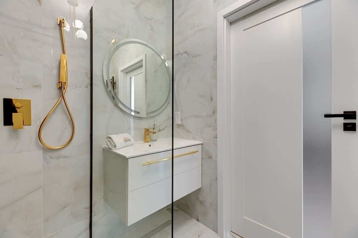 A modern bathroom with a glass-enclosed shower, a white vanity with gold handles, and a large mirror.