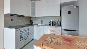 Et moderne køkken med hvide skabe, indbygget ovn, et rustfrit stål køleskab og et træspisebord med vævede servietringe.