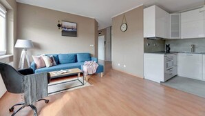 En moderne lejlighed med en blå sofa, et spisebord, et køkken med hvide skabe og et ur på væggen.