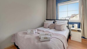 Et hotelværelse med seng, et natbord, et vindue med gardiner og udsigt til bygninger.