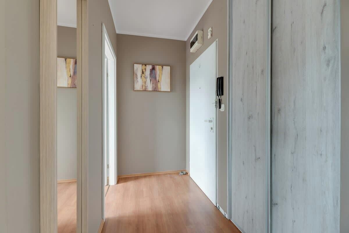 Un pasillo con suelo de madera, una puerta con un teléfono y dos cuadros abstractos en la pared.