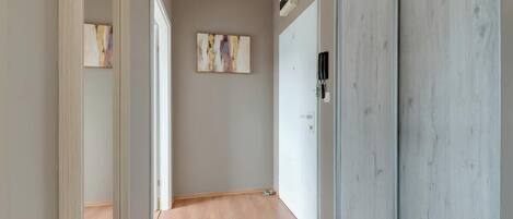 Un pasillo con suelo de madera, una puerta con un teléfono y dos cuadros abstractos en la pared.