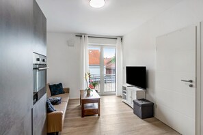 Ein modernes Wohnzimmer mit Sofa, Couchtisch, Flachbildfernseher und Küchenzeile mit Herd.