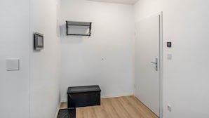 Una stanza con una porta bianca, un mobile contenitore nero, una mensola a muro, un termostato e un interruttore della luce.