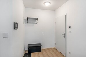 Ein Zimmer mit weißer Tür, schwarzem Stauraum, einer Wandablage, einem Thermostat und einem Lichtschalter.