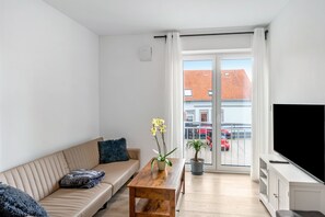 A modern living room with a sofa, a coffee table, a TV, and a balcony with a view of the city. - Apartment 'Haus Seeluft – W6' with Wi-Fi (Butjadingen)