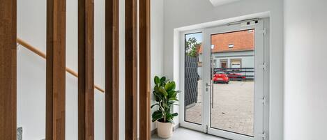 A modern interior with a wooden staircase, a potted plant, and a view of a red car outside through a glass door.