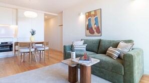 A modern living room with a green sofa, a wooden coffee table, a dining area with a white table and chairs, and a kitchen in the background. - Cozy Porto Home w/ AC by LovelyStay (Porto)
