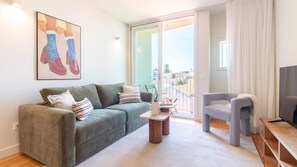 Ein Wohnzimmer mit einem grünen Sofa, einem grauen Sessel, einem kleinen Holztisch und einem Fernseher.