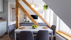 Un espace repas avec une table blanche, des chaises grises et une structure de poutres en bois au plafond.