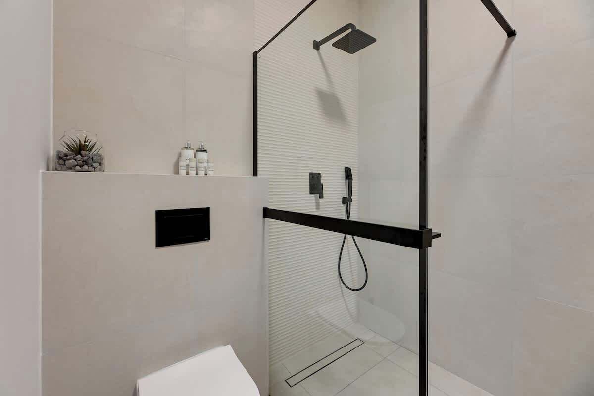 Un baño moderno con cabina de ducha de vidrio, un lavabo blanco y una pequeña repisa con artículos de aseo.