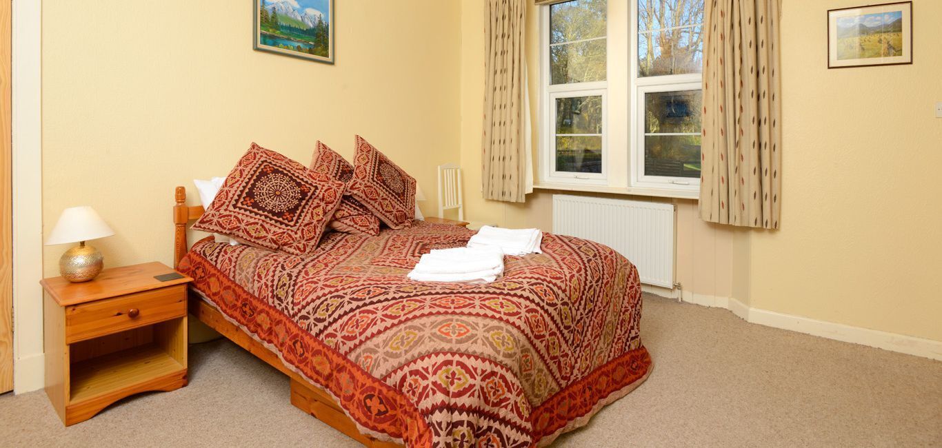 A bedroom with a bed, a nightstand, a window with curtains, and a radiator.