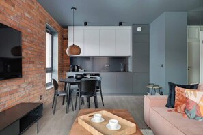 Um espaço de estar moderno com parede de tijolos, televisão de tela plana, área de refei ções com cadeiras, cozinha com armários e um sofá com almofadas.