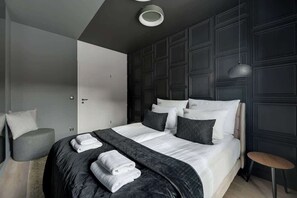 Quarto moderno com cama grande, mesa de cabeceira, cadeira e guarda-roupa.