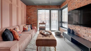A modern living room with a brick wall, a large TV, a sofa, and a coffee table. - Scala 220 with Balcony | City Center | Parking (Gdańsk)