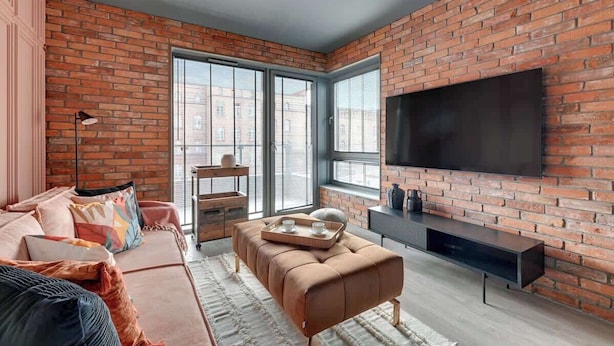 A modern living room with a brick wall, a large TV, a sofa, and a coffee table. - Scala 220 with Balcony | City Center | Parking (Gdańsk)