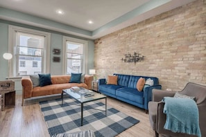 A living room with a brick wall, two sofas, a coffee table, and a checkered rug. - Casa Sherbourne Hotel - Modern Industrial Suite (Toronto)