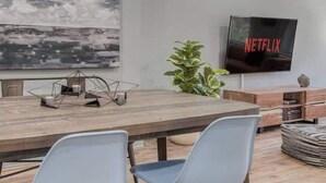 Una sala de estar moderna con comedor, televisor de pantalla plana y un cuadro abstracto grande.