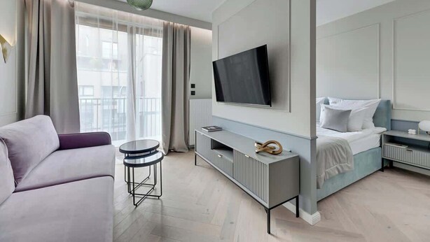 A modern hotel room with a sofa, a TV mounted on the wall, a bedside table, and a bed. - Nadmotławie B36 | Riverside & Gym (Gdańsk)