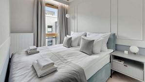 A hotel room with a large bed, a bedside table, a nightstand, a window with curtains, and a view of a building outside. - Nadmotławie B36 | Riverside & Gym (Gdańsk)
