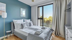A modern bedroom with a large bed, a bedside table, a floor lamp, and a view of the outdoors. - Tarasy Bałtyku 5 | Seaside | Billard, Sauna & Gym (Gdańsk)