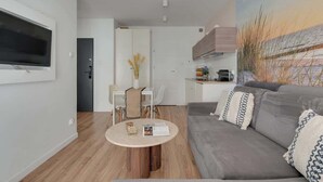 Ein modernes Wohnzimmer mit einem grauen Sofa, einem runden Couchtisch und einem an der Wand befestigten Fernseher.