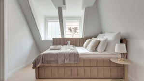 A bedroom with a sloped ceiling, a bed with a headboard, a bedside table, and a window. - Main Old Town & Family Stay | Długa Street (Gdańsk)