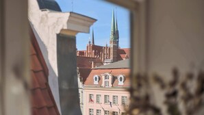 A view of a building with a pointed green spire and a red-tiled roof through a window. - Main Old Town & Family Stay | Długa Street (Gdańsk)