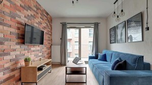 Un salon avec un mur en briques, un téléviseur à écran plat, un canapé bleu et une table basse.