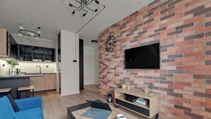 Un espace de vie moderne comprenant une cuisine, un coin repas avec un ordinateur portable et une tasse, et un téléviseur fixé à un mur en briques.