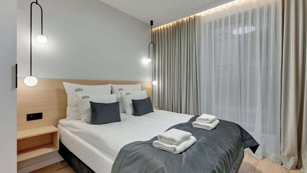 A modern hotel room with a neatly made bed, bedside tables, and a large window with sheer curtains. - Grano Residence 1 | Riverside | Parking (Gdańsk)