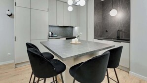 A modern kitchen with a central island, black chairs, and a pendant light. - Grano Residence 1 | Riverside | Parking (Gdańsk)