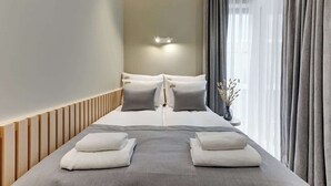 Una camera d'albergo con un letto, cuscini, un comodino con un vaso e una finestra con tende.