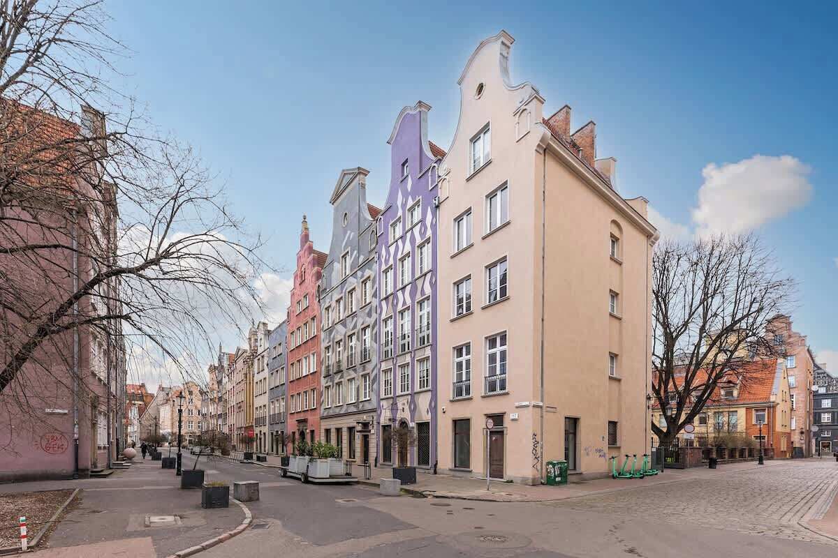 Una hilera de edificios de varios pisos con una calle adoquinada, cielo despejado y árboles sin hojas.
