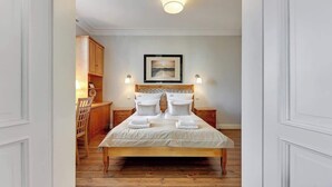Een slaapkamer met een houten bed, witte beddengoed, een hoofdbord met decoratieve details, een ingelijst kunstwerk aan de muur en een klein tafeltje met een lamp.