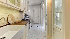 Een smalle keuken met witte kastjes, een zwart-wit betegelde vloer en een houten aanrecht.