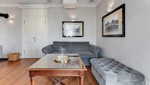 Een woonkamer met een salontafel met glazen blad, grijze banken en een gestofte grijze bank.