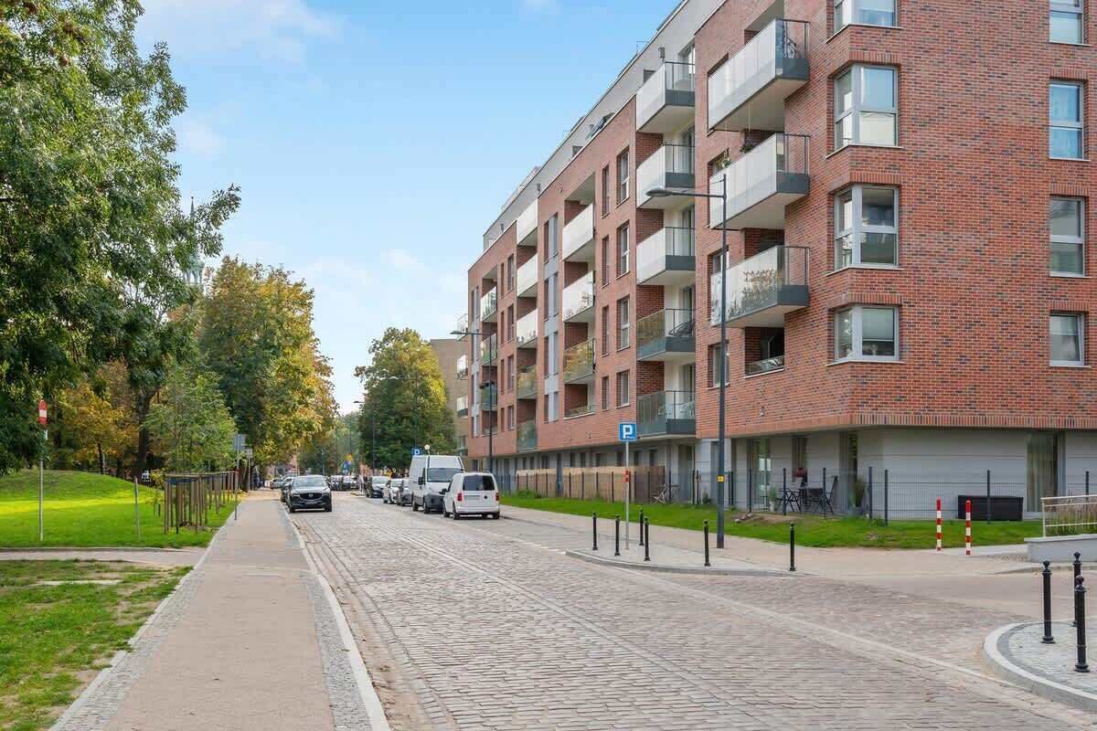 A multi-story residential building with a brick facade, balconies, and a paved street with parked cars.