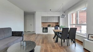 A modern living space with a sofa, dining table, chairs, and a kitchen area. - Bastion Wałowa 10 | City Center | Parking (Gdańsk)